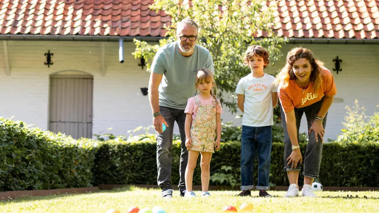 Une famille s'amuse dans le jardin avec un jeu de pétanque en ligne. Les boules colorées sont alignées sur l'herbe.