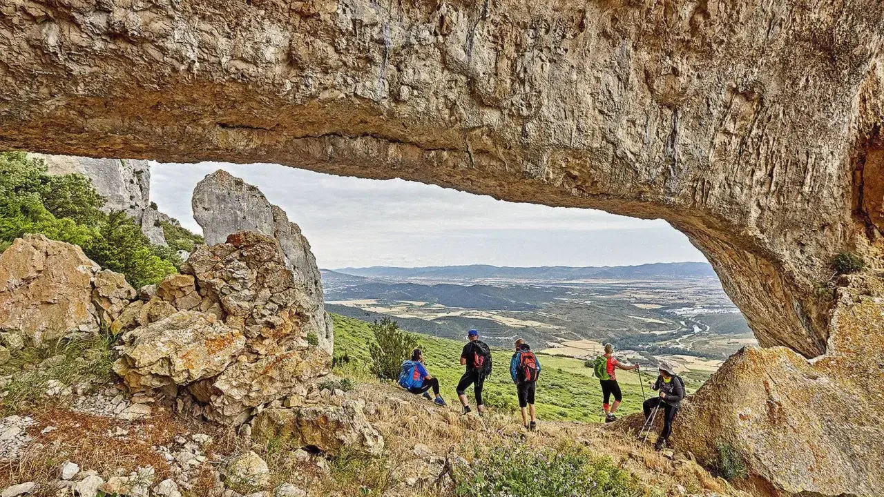 Senderismo Navarra: grupo de excursionistas admira un paisaje montañoso desde debajo de un arco de roca natural.