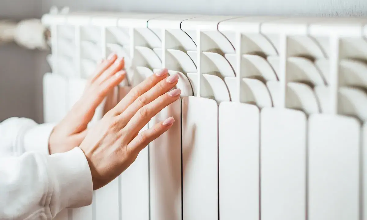 Manos cálidas sobre un convector blanco, sintiendo el calor del invierno.