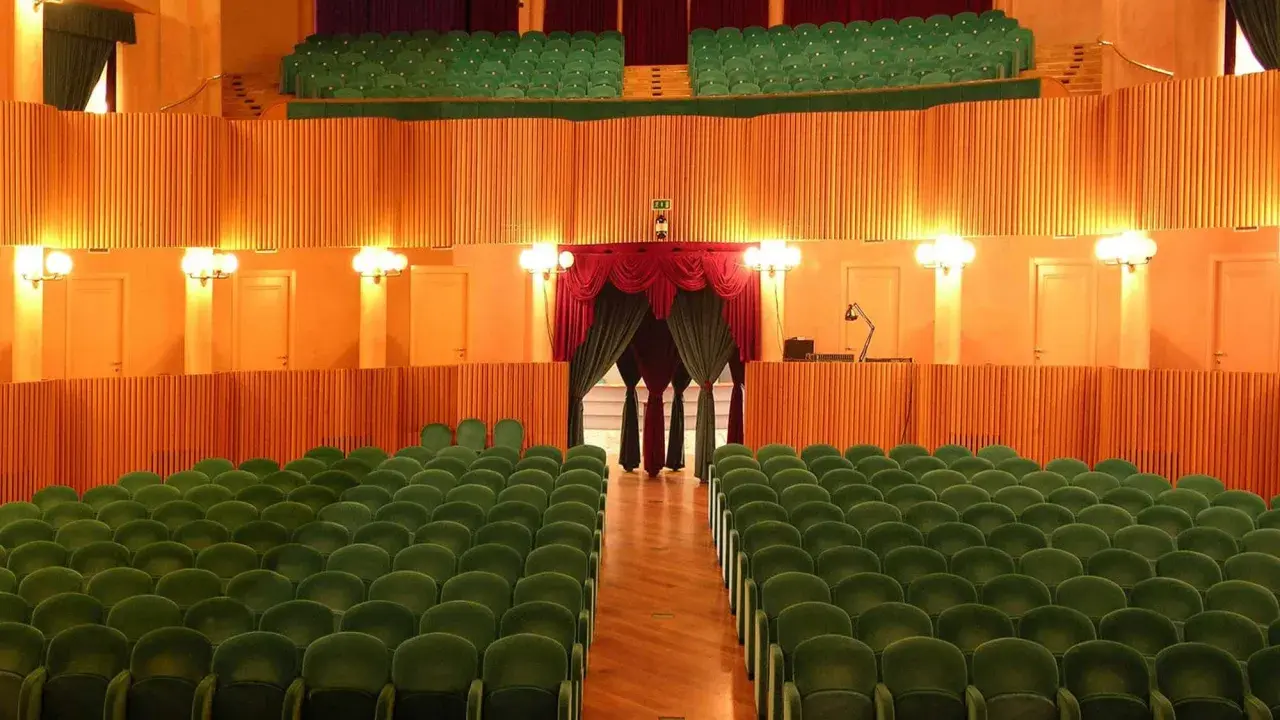 L'arena della regina cattolica, un teatro con poltrone verdi e sipario rosso, attende il pubblico.