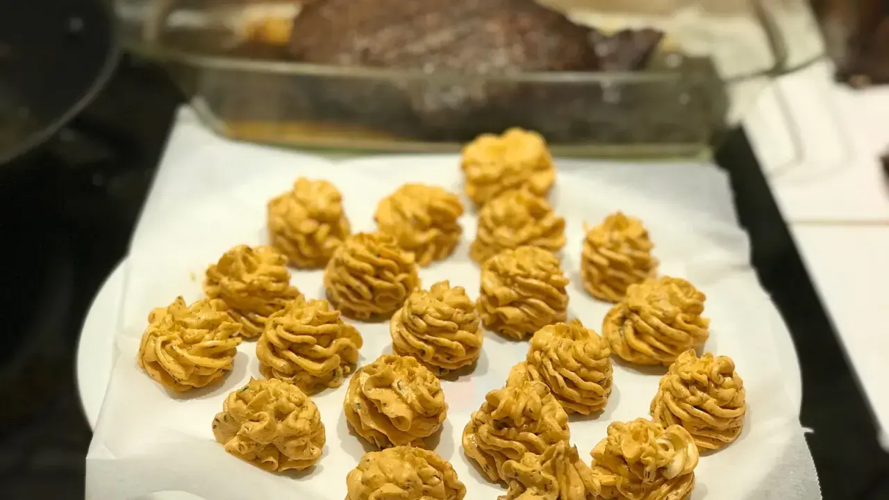Piped dollops of golden-brown sauce arranged on white parchment paper, with a roasted dish in the background.
