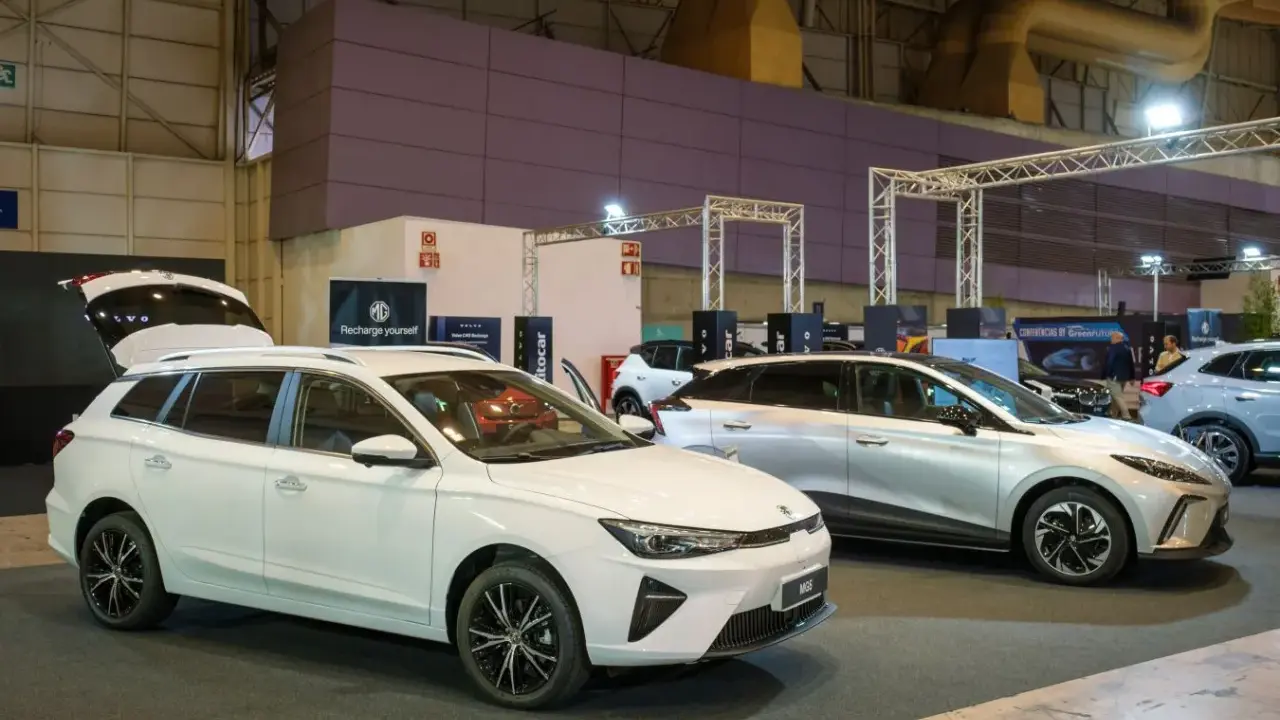 Białe kombi MG5 z otwartą klapą bagażnika i srebrny SUV na wystawie samochodowej.