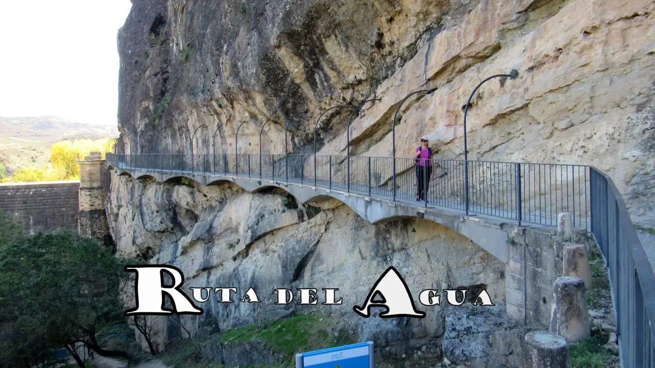 Un pontón de la oliva, parte de la Ruta del Agua, se aferra a un acantilado rocoso. Una mujer camina por el sendero con barandillas.