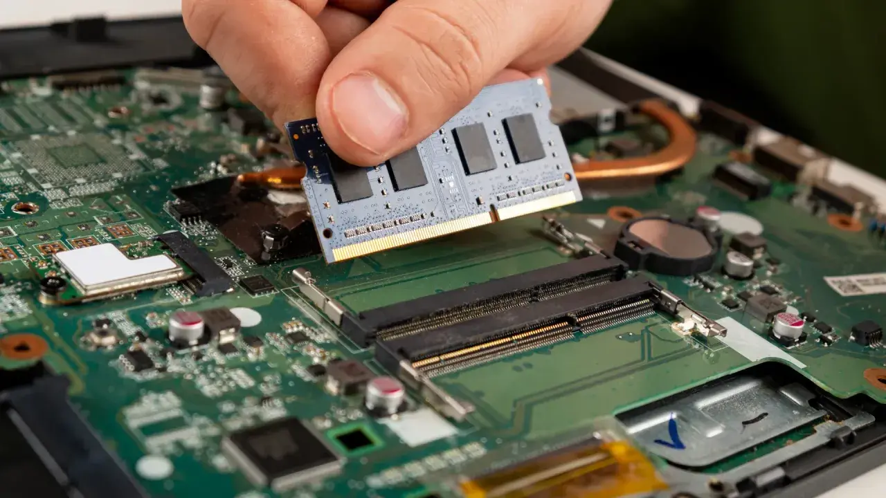 Main d'une personne installant un module de test RAM sur une carte mère d'ordinateur portable.
