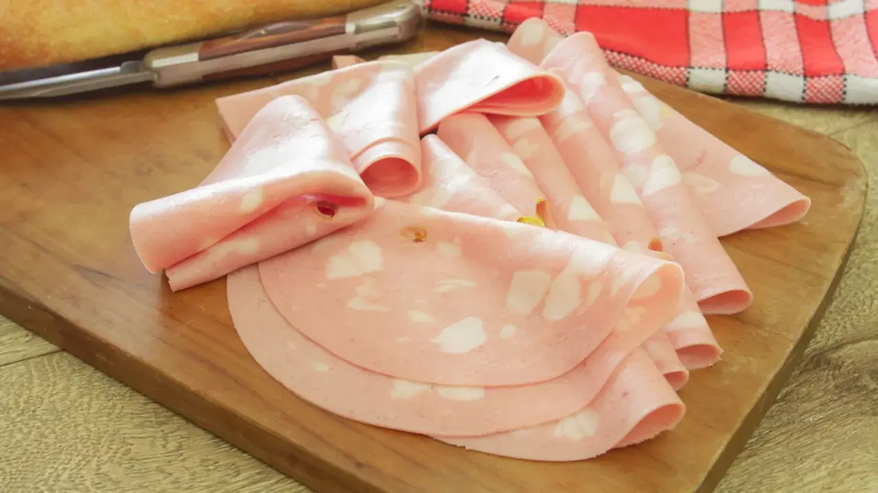 Fette di salame rosa, come in attesa di un lieto evento, disposte su un tagliere di legno.