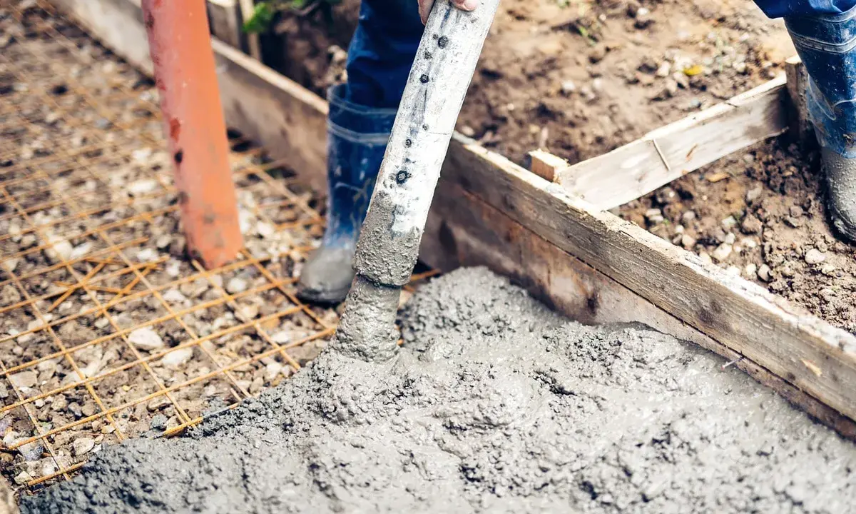 Arbeiter betonieren bei Regen eine Fundamentplatte. Beton fließt aus einem Schlauch auf eine Bewehrung.