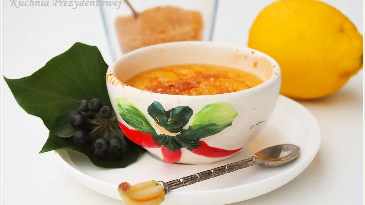 Słodka, karmelizowana crema catalana w ozdobnej miseczce, obok cytryna i jagody.