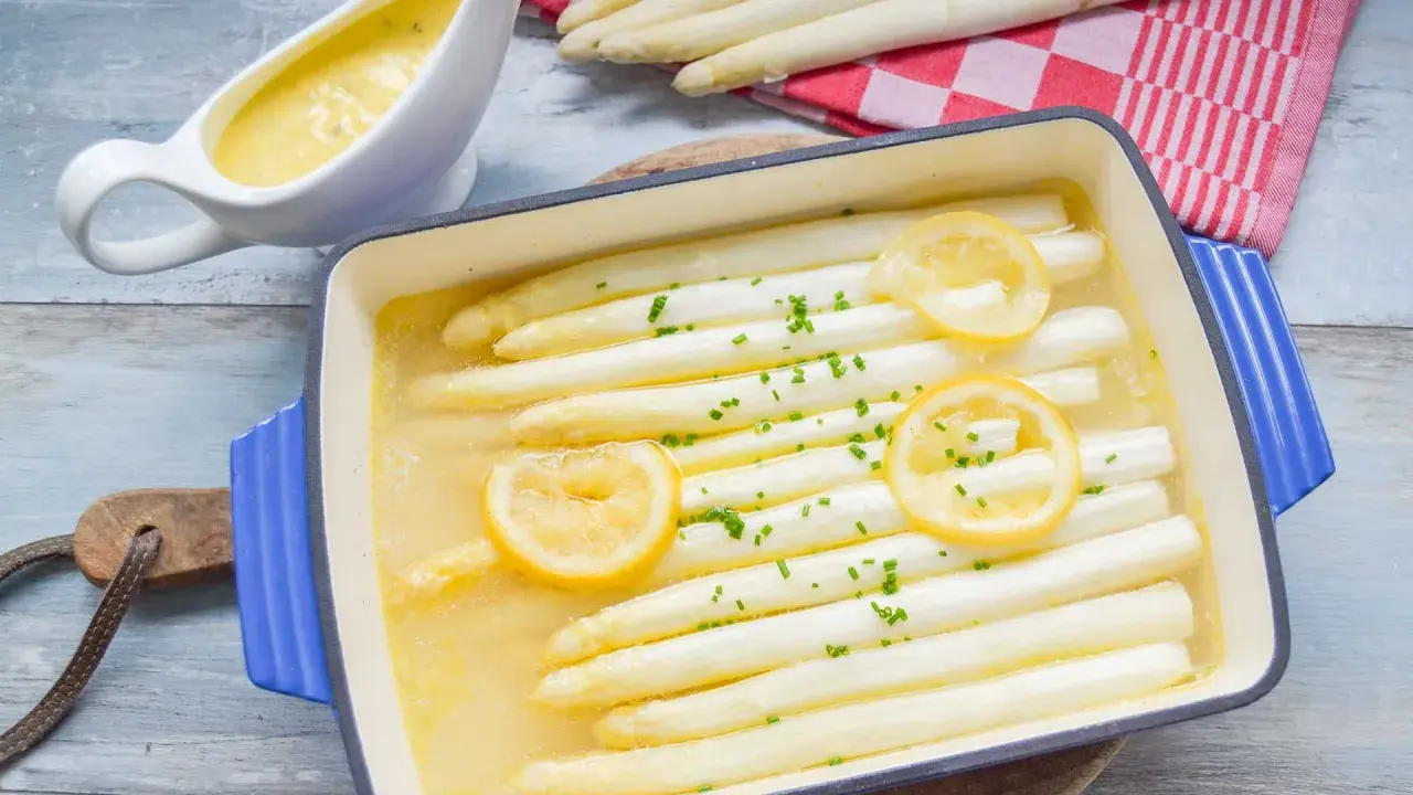 Weißer Spargel in einer Auflaufform mit Zitrone und Kräutern, daneben eine Sauciere mit Sauce.