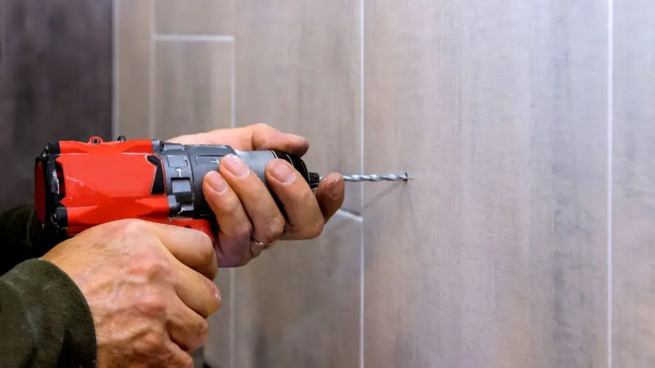 Man usa una broca para azulejo con un taladro para hacer un agujero en una pared de azulejos.