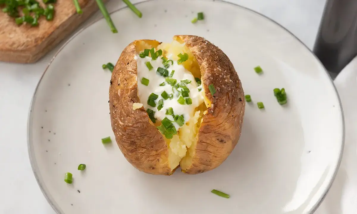 Patatas asadas en freidora de aire, crujientes por fuera, tiernas por dentro, coronadas con crema agria y cebollino fresco.