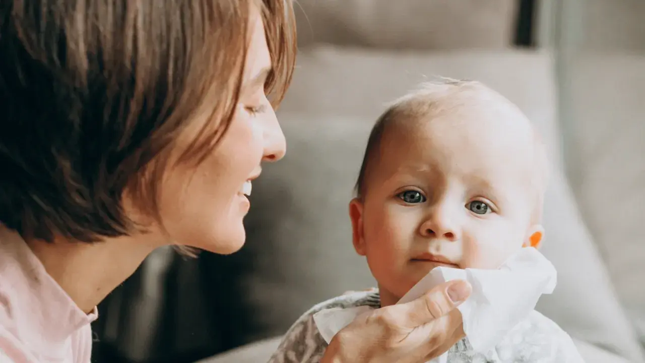 Mama delikatnie wyciera buzię dziecka, które ma żółty katar.