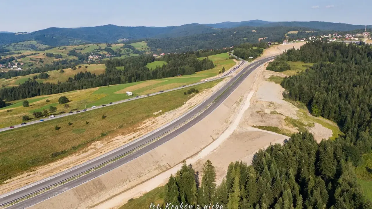 Nowa droga 47 przecina malownicze, zielone wzgórza. Widać ruch samochodów i lasy.