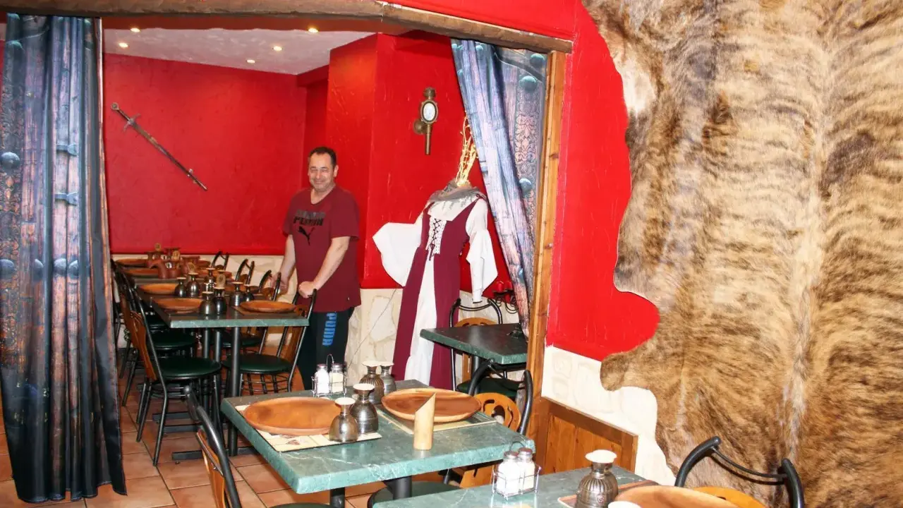 Un homme se tient dans un restaurant moyen âge décoré d'une peau d'ours et d'une épée.