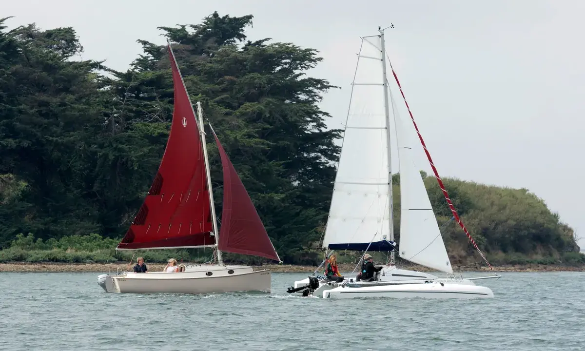 Deux voiliers naviguent sur l'eau, l'un avec une voile rouge, l'autre avec une voile blanche. On dirait un **bateau corsaire** prêt pour l'aventure.