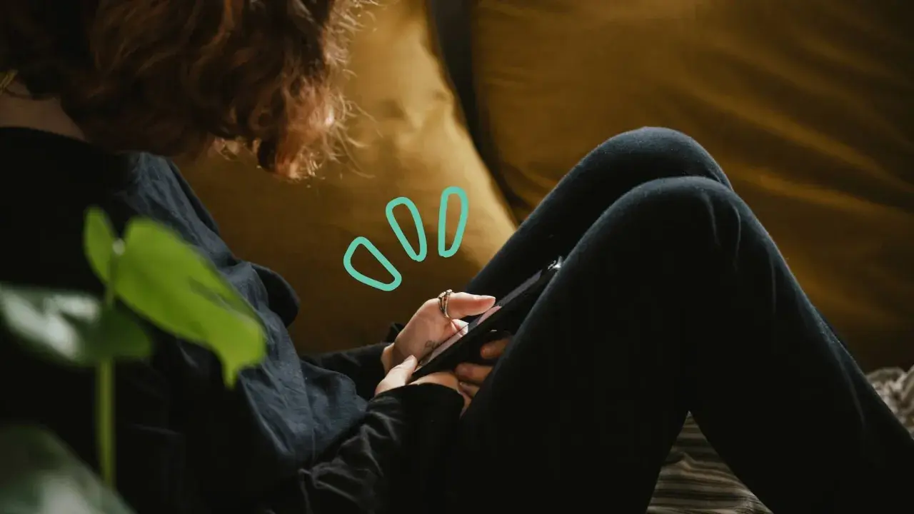 Une personne aux cheveux roux utilise son smartphone, symbolisant quelles peuvent être les principales conséquences de la cyberdépendance : isolement, anxiété, perte de temps.