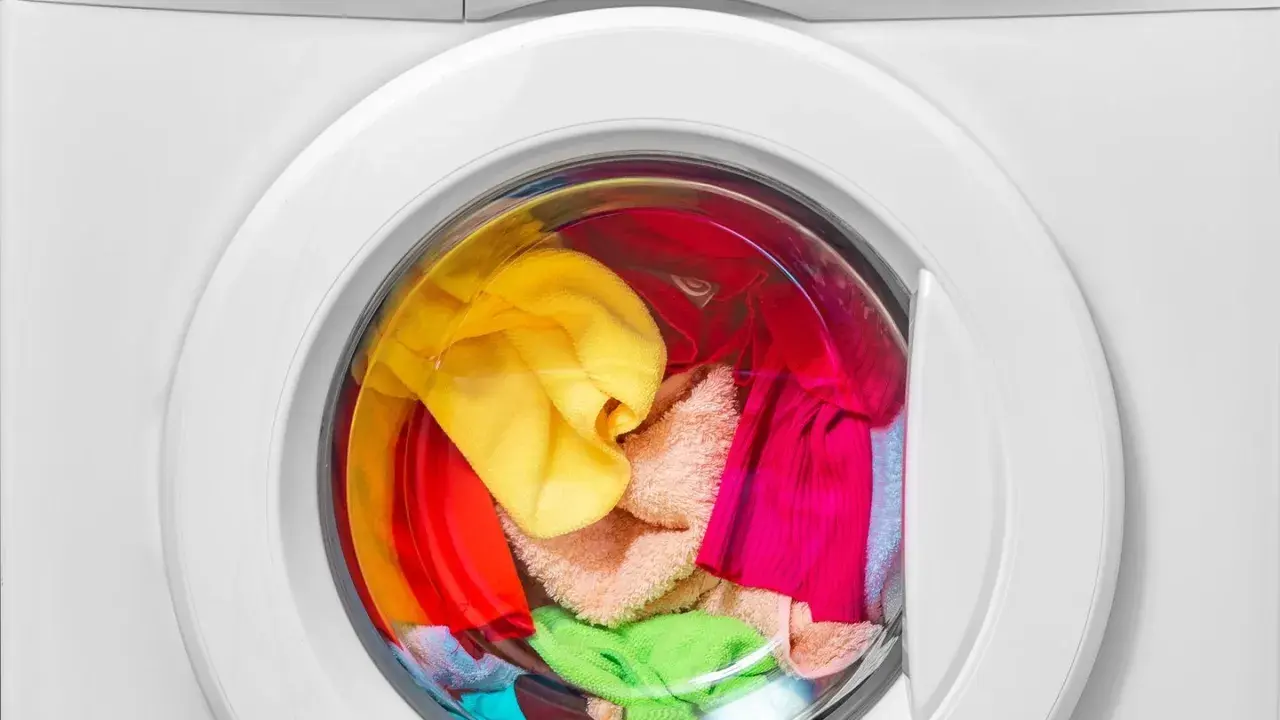 Bunte Wäsche, darunter ein gelber und ein grüner Schwamm, wartet in der Waschmaschine auf das schwamm waschen.