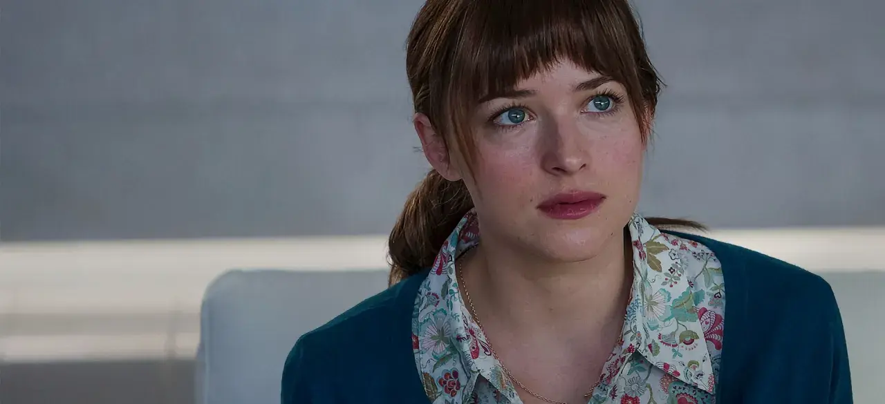 Dakota Johnson med sina blå ögon och blonda hår, klädd i en blommig skjorta och en mörkblå kofta. En scen från filmer med Dakota Johnson.