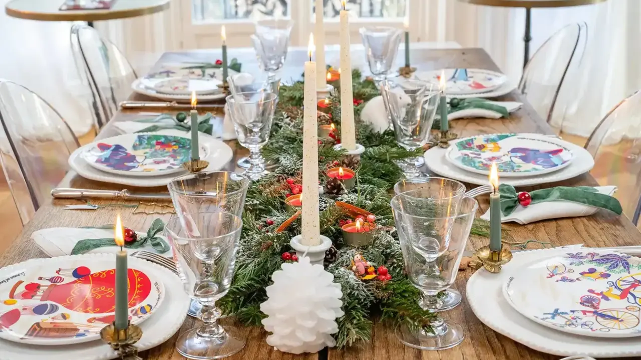 Une table dressée pour les fêtes, avec des assiettes décorées, des bougies allumées et une guirlande de sapin, évoquant la magie des arts de la table.