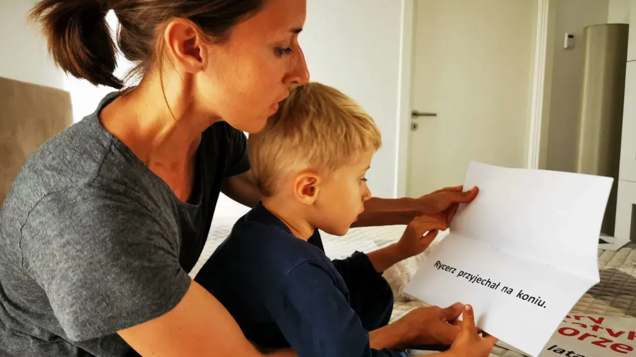 Mama pomaga synkowi w nauce czytania. Razem czytają zdanie "Rycerz przyjechał na koniu".