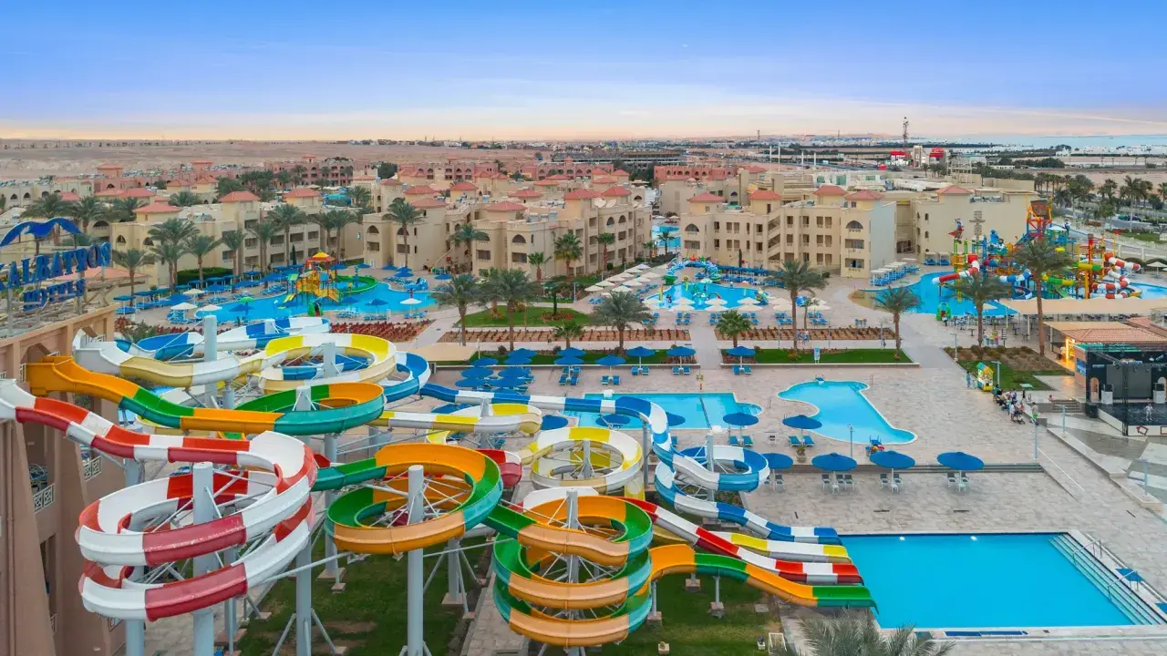 Kolorowe zjeżdżalnie wodne i baseny w Albatros Aqua Park, otoczone palmami i hotelami, zapraszają do zabawy.