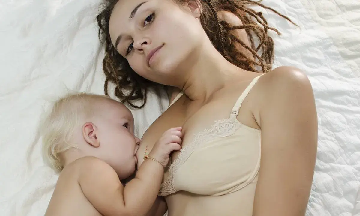 Mama z dredami karmi piersią niemowlę. To piękny moment bliskości, choć nie jest to karmienie piersią 10 latka.
