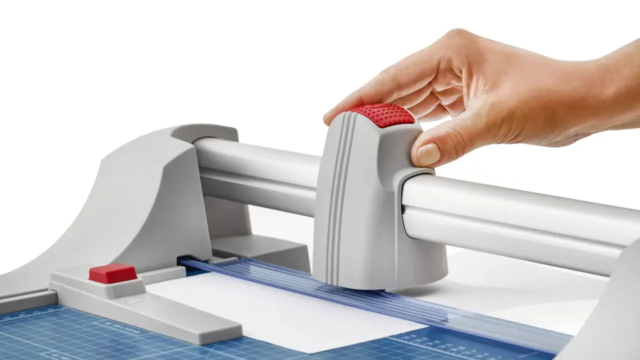 Mano operando una guillotina o cizalla para cortar papel con precisión.