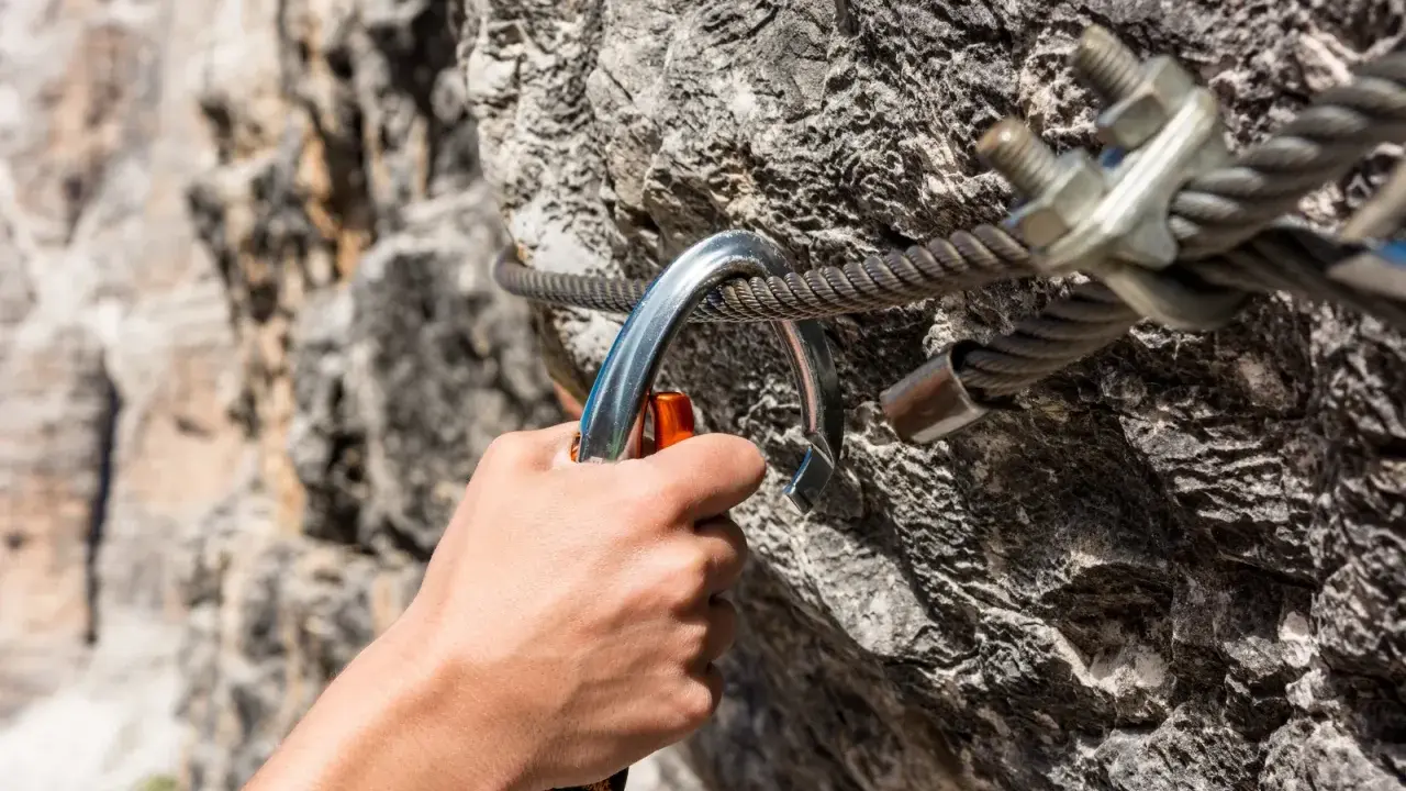 Dłoń zapina karabinek do stalowej liny na via ferrata. Bezpieczeństwo podczas wspinaczki.