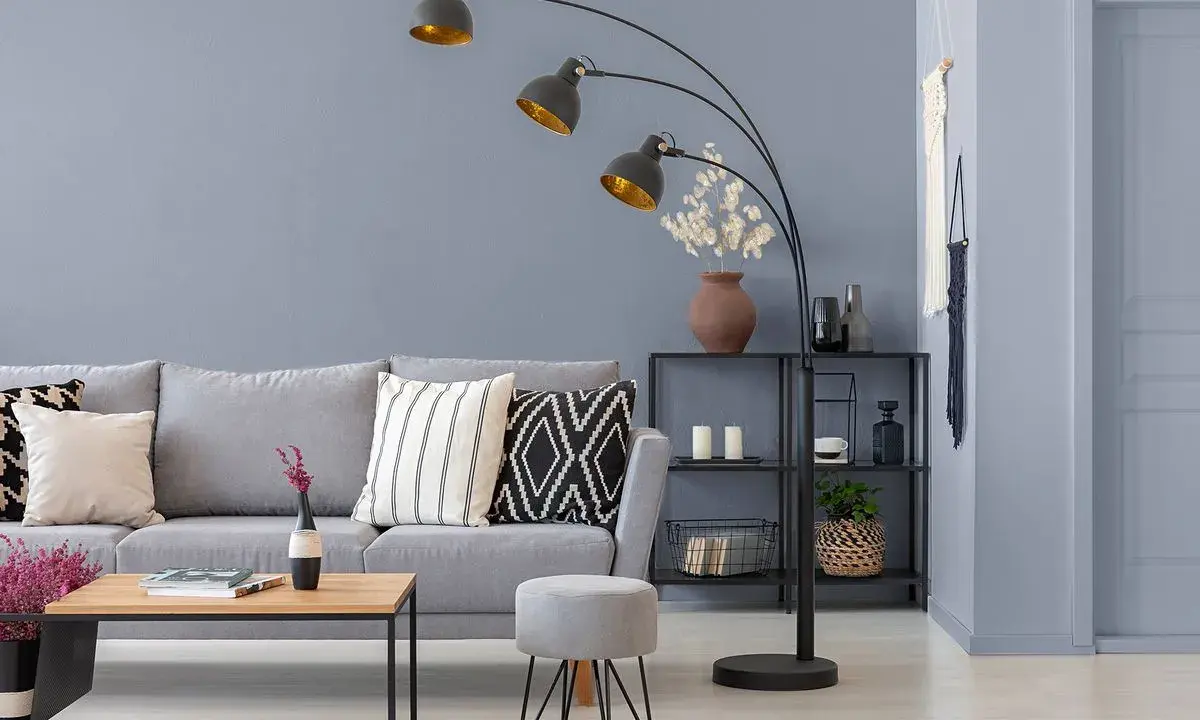 Przytulny salon z szarą kanapą, stolikiem kawowym i łukową lampą. Ciepły szary kolor ścian tworzy relaksującą atmosferę.