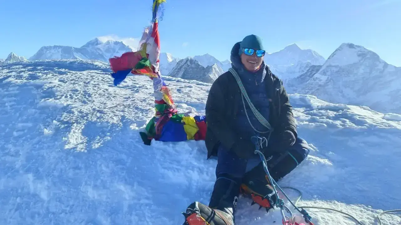 Szczęśliwy alpinista na szczycie Mera Peak, otoczony śniegiem i modlitewnymi flagami, z majestatycznymi górami w tle.