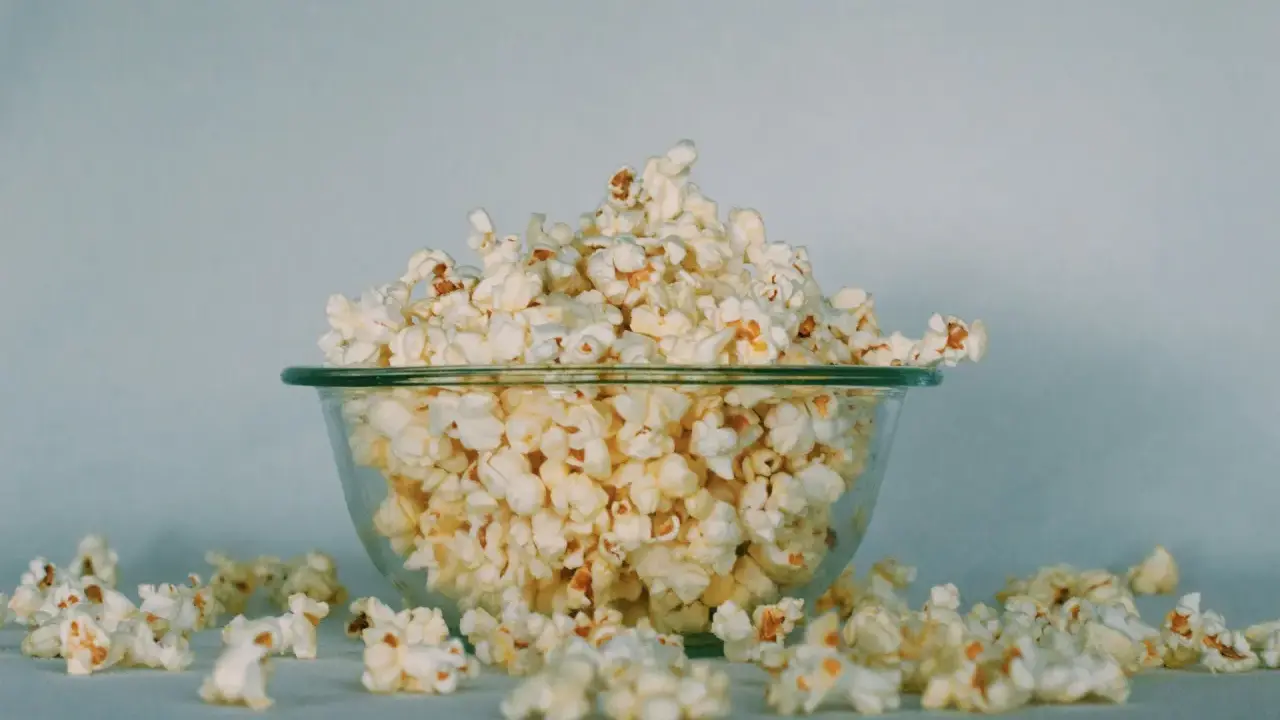 Góra popcornu w szklanej misce, rozsypane ziarna wokół. Ile popcorn kcal?