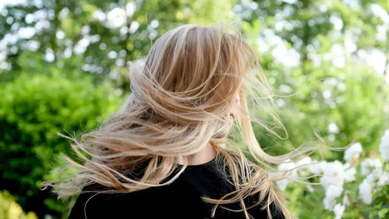 Warkocze wiatru rozwiewają chłodny blond włosów dziewczynki na tle zieleni.