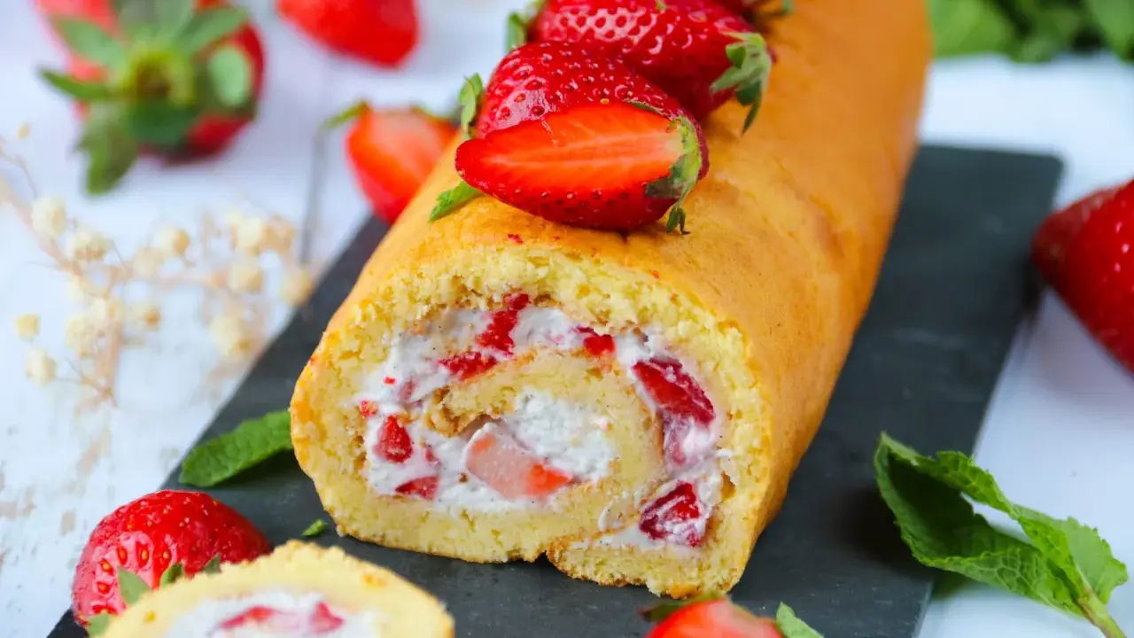 Un roulé aux fraises moelleux, garni de crème et de morceaux de fraises fraîches, décoré de fraises entières.