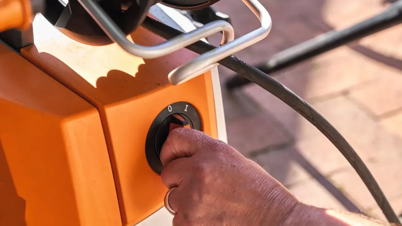 Hand dreht Schalter am orangefarbenen Hochdruckreiniger. Vorbereitung zum Anschluss an den Wasserhahn.