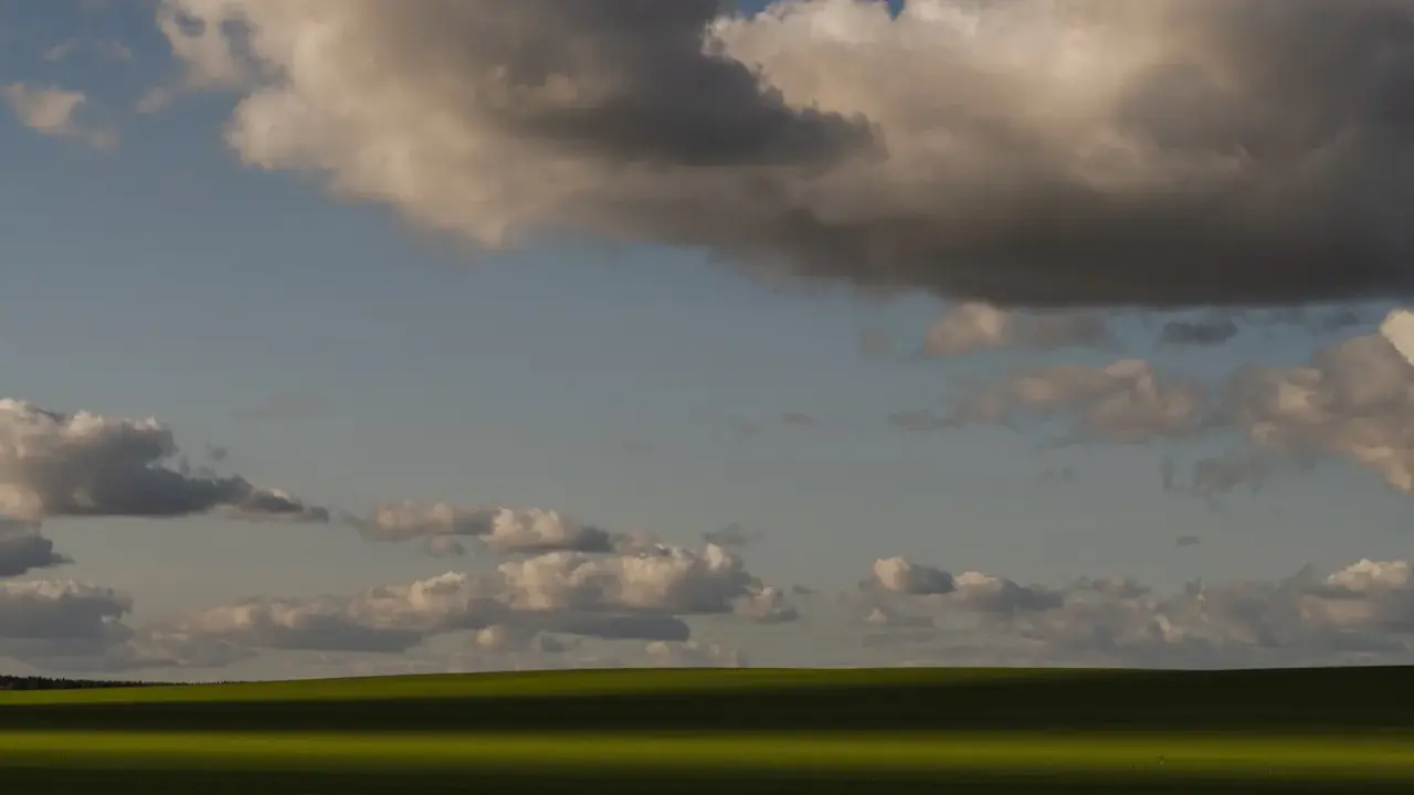 Zachód słońca nad zielonym polem, rzucającym długi cień. Chmury na niebie tworzą ciekawe fotografie.
