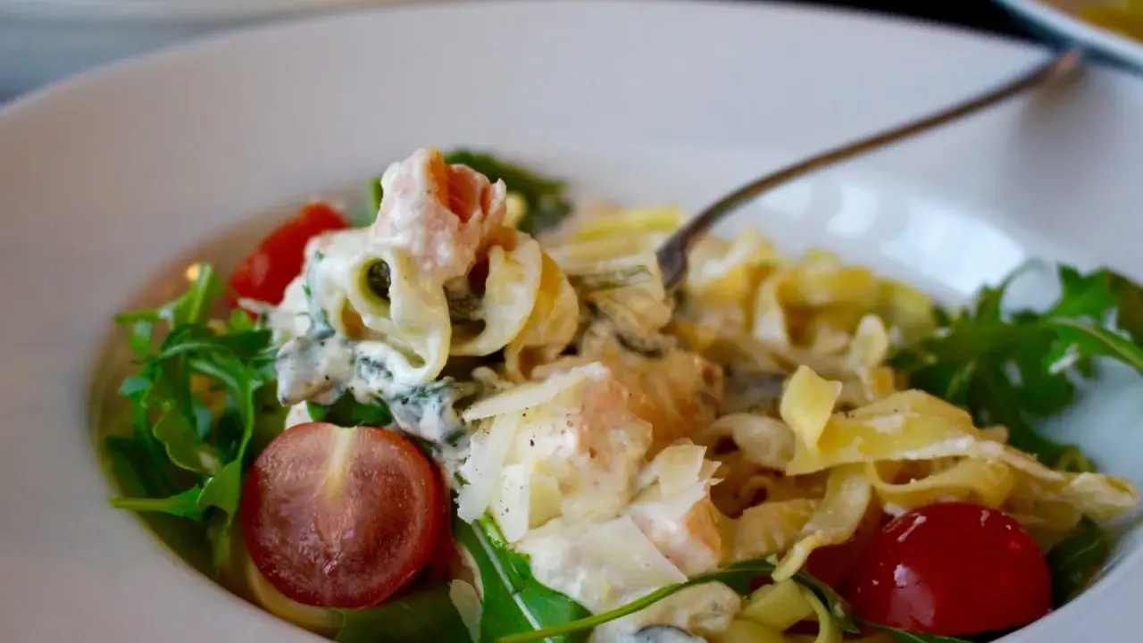 En krämig laxpasta med spenat, körsbärstomater och ruccola. En gaffel lyfter upp en bit av den läckra pastan.