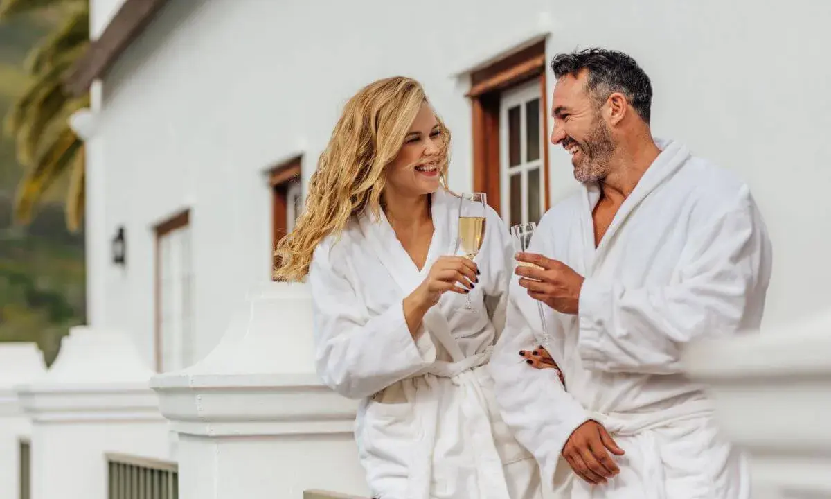 Para relaksu w hotelach spa w Polsce. Uśmiechnięta para w szlafrokach wznosi toasty szampanem na balkonie.