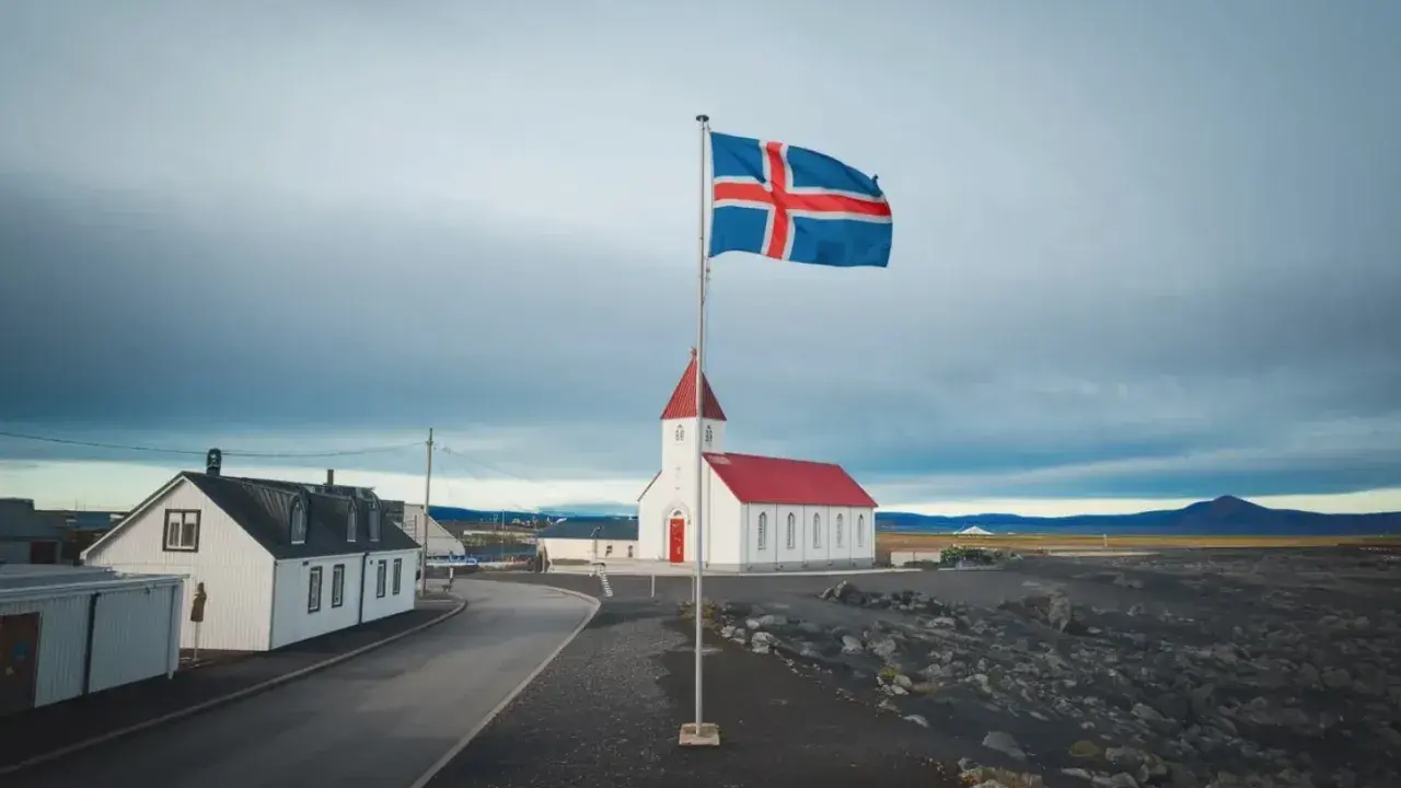 Islandia praca: biały kościół z czerwoną wieżą i flagą Islandii na tle pochmurnego nieba.