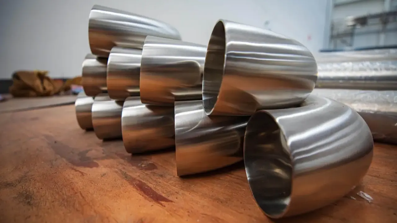 Pièces métalliques brillantes, probablement des coudes pour un poêle à bois conduit, empilées sur une surface en bois.