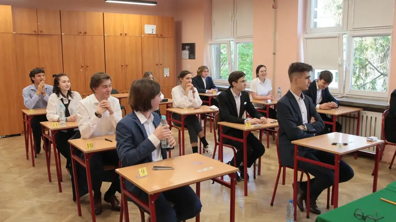 Uczniowie siedzą w ławkach podczas egzaminu. Zastanawiają się, ile trwa matura z biologii, skupieni na zadaniach.