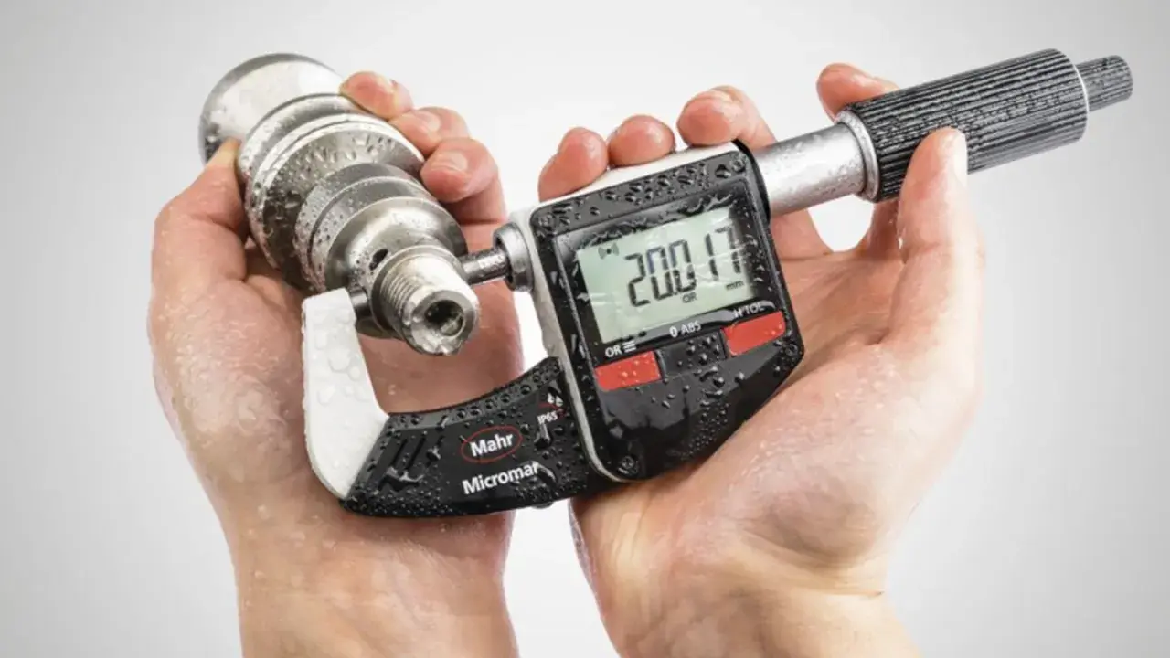 Manos sostienen un micrometro digital Mahr Micromar, midiendo una pieza metálica. La pantalla muestra 200.17 mm.