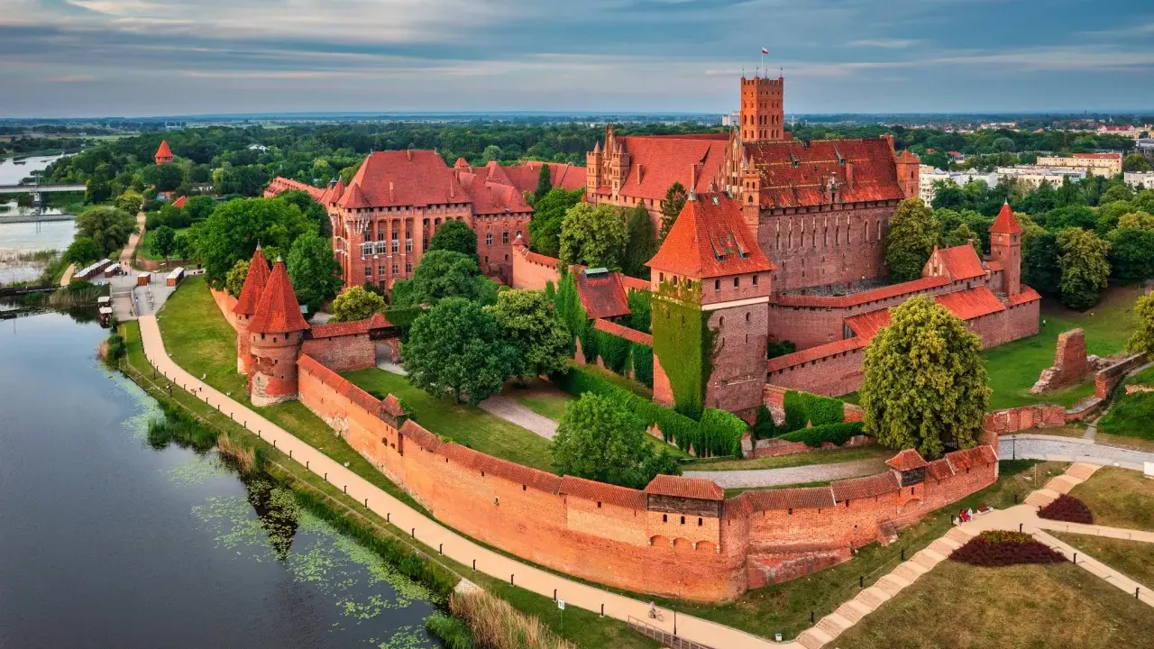 Potężny zamek w Malborku, jedna z największych atrakcji Polski, otoczony murami obronnymi i rzeką Nogat.