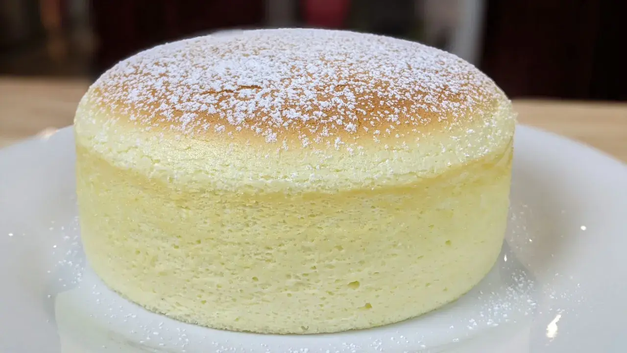 Un délicieux cheesecake japonais, léger et aérien, saupoudré de sucre glace sur une assiette blanche.