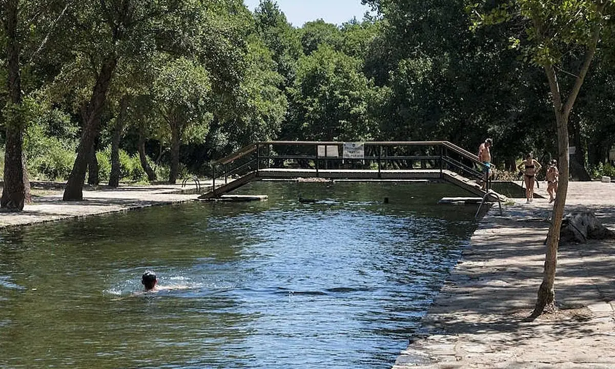 Un día soleado en las piscinas naturales de La Codosera. Personas disfrutan del agua fresca, una nada mientras otras pasean por la orilla.