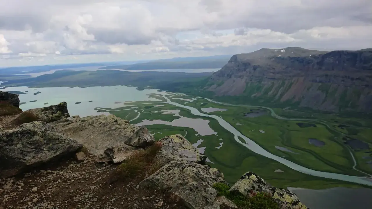 Vacker utsikt över Rapadalen med Skierfe i bakgrunden. En slingrande flod flyter genom ett grönt landskap med sjöar.