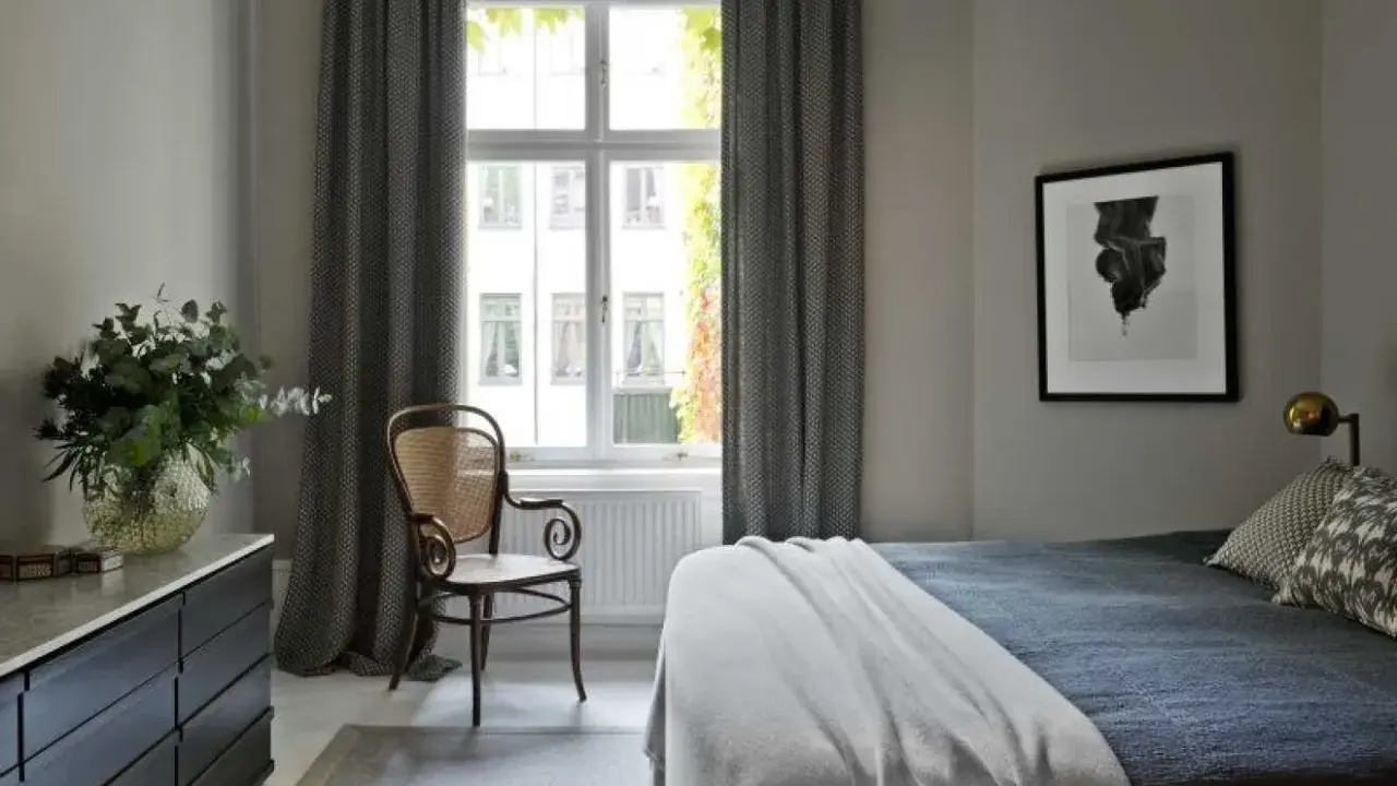 Sovrum med en säng, en stol och en byrå. Konst av Sofia Wallenstam på väggen.