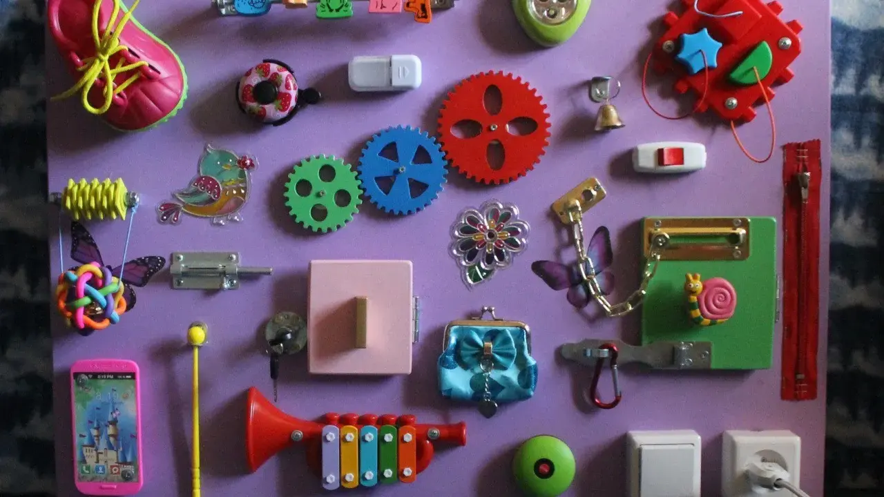 Lavagna sensoriale fai da te con scarpa, ingranaggi, campanello, lucchetto e altri elementi per stimolare i bambini. Perfetta per giochi montessori 2 anni fai da te.