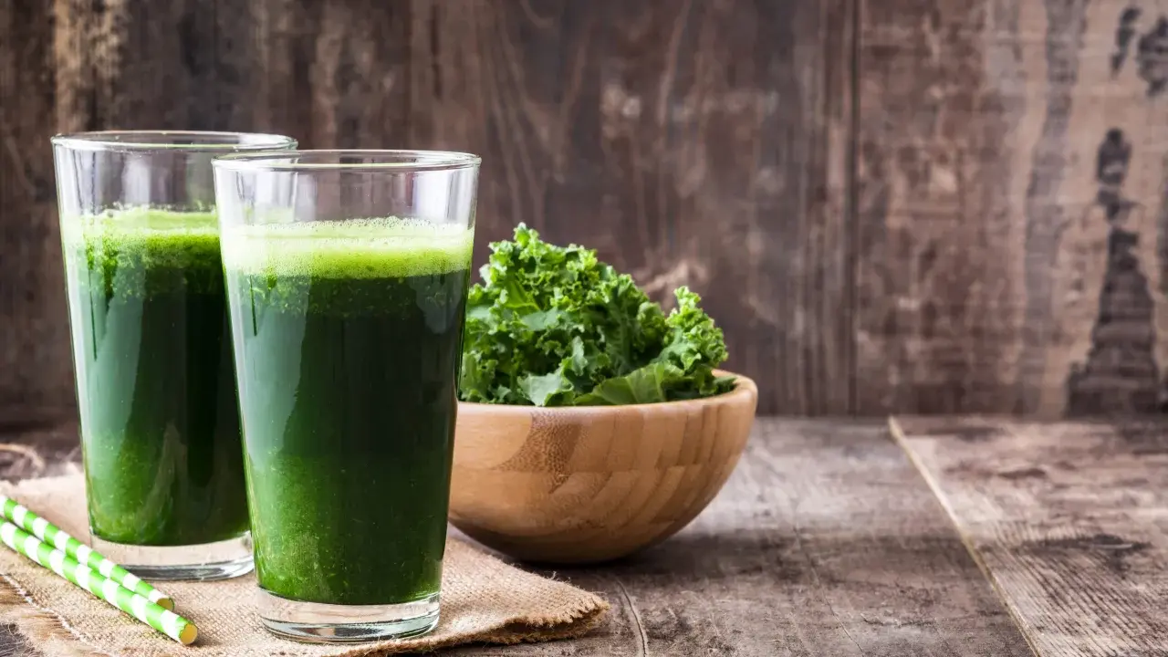 Dwa szklanki zielonego smoothie, miska jarmużu i słomki. Idealne na śniadanie zgodne z dietą sirtuinową.