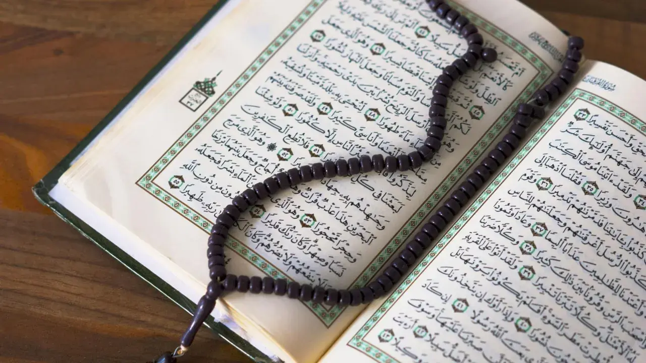 Ein Koran mit Perlenkette liegt auf einem Holztisch. Die Seiten sind mit arabischer Schrift bedruckt, die an die Geschichte von Yajuj und Majuj im Islam erinnert.
