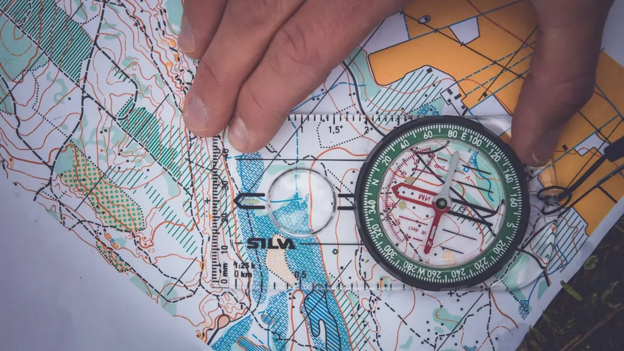 En hand håller en kompass över en karta, vilket visar hur fungerar en kompass för orientering.