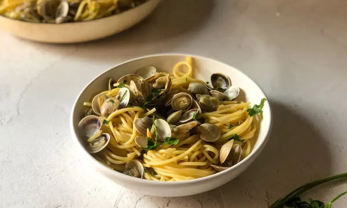 Un invitante piatto di spaghetti alle vongole, con pasta dorata e molluschi freschi, guarnito con prezzemolo.
